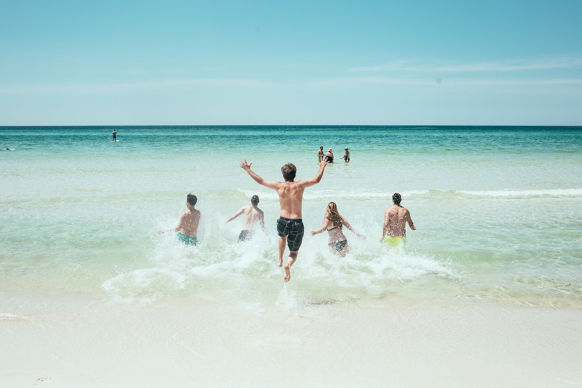 group of friends running into the ocean on a sunny day